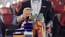 Stewardess take water bottle from trolley cart in passenger cabin of airplane jet. Modern plane interior. Cropped image of woman wear uniform. Civil commercial aviation. Air travel concept�