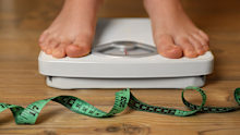 Overweight girl using scales near measuring tape on wooden floor, closeup