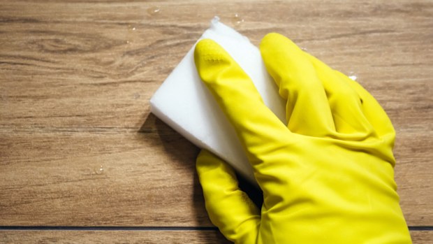 A hand in a yellow rubber glove cleaning with a magic eraser