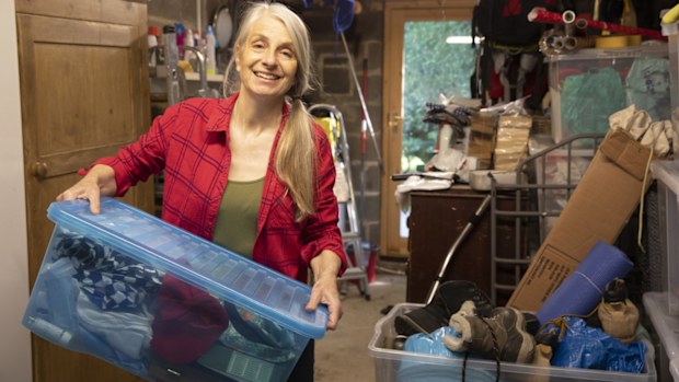 A mature woman smiles as she carries boxes of belongings to sort through whilst in lockdown at home.