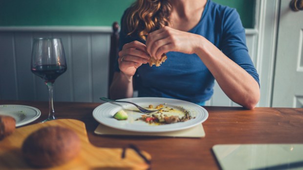 A young woman is seated at a table and is eating a meal of bread and wine alone