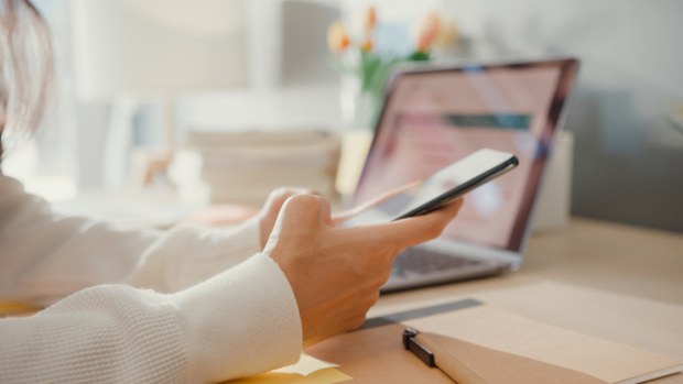 Close-up young lady freelance focus mobile phone chat with colleagues work finance graph account chart market plan in laptop at home. Girl student learn online at house, Work from home concept.