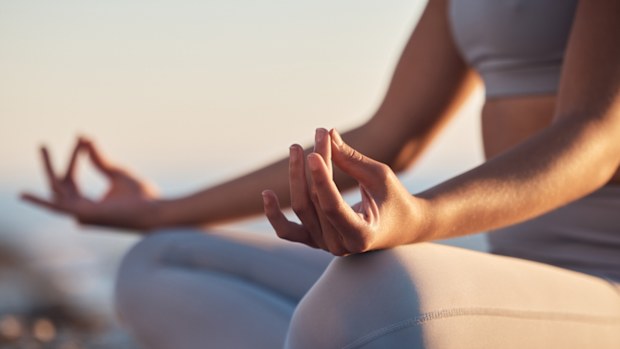 Woman, hands or lotus pose meditation on sunset beach, ocean or sea in mental health, mind training or chakra balance. Zoom, peace or zen yogi in calm mudra, relax yoga wellness or sunrise gratitude