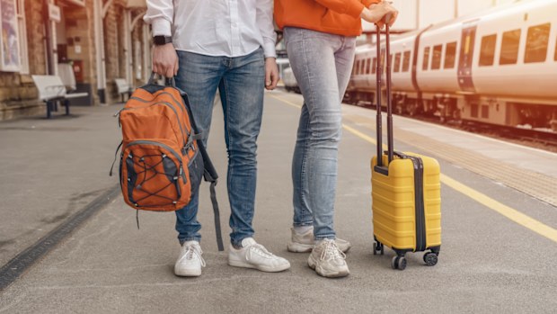Travelers with a backpack and yellow suitcase waiting for a train at the train station. The couple missed the train. Travel concept.