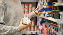 A woman choosing canned dog or cat food at a pet store, reading the label. Customer compares wet dog or cat food in the aisle with various canned foods on the shelves. Concept of responsible pet owner