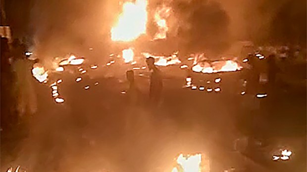In this image made from video, people walk by burning debris following the explosion of an oil tanker in the Wellington suburb of Sierra Leone's capital Freetown.