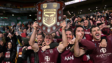 Daly Cherry-Evans lifts the Origin shield to the delight of the Maroons fans in the stand right behind him.