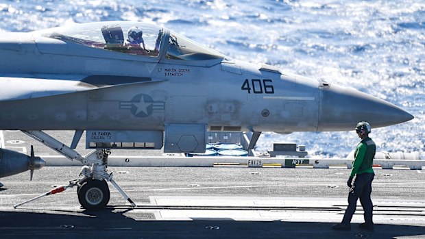 A green shirt 'Hook Runner' crew member moves a Super Hornet into position prior to launching
