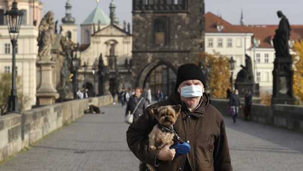 A man wearing a face mask carries his dog across the medieval Charles Bridge in Prague, Czech Republic, Wednesday, Oct. 21, 2020