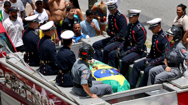 The Brazilian flag-draped coffin of football legend Pelé is transported atop a fire truck in a funeral procession through the streets of Santos.