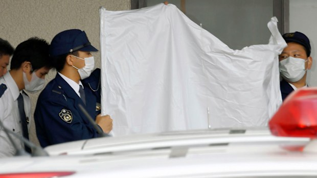 Police officers hide the face of arrested Japanese Yoshitane Yamasaki with a sheet while escorting him to a police vehicle to leave for Prosecutor's Office for further investigation, in Sanda City, western Japan. (AAP)