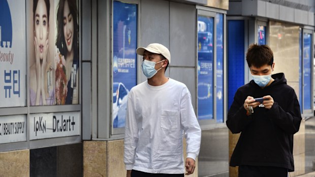 Zhang Bin, right, walks with a friend along a street, both wearing protective masks in the Koreatown section of Los Angeles.