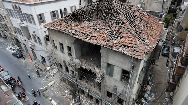 People pass in front of a house that was damaged during the last week's explosion that hit the seaport of Beirut, Lebanon, Tuesday, Aug. 11, 2020