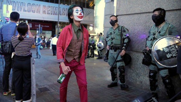 A man in a Halloween costume walks past police officers in riot gear in Hong Kong.