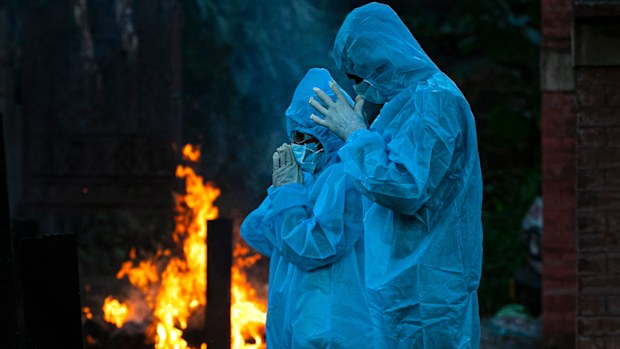 A nine-year-old boy, left, in personal protective equipment offers prayers during the cremation of his father who died of COVID-19 in Gauhati, India.`