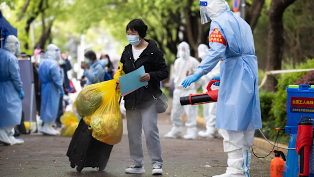 A villager carrying baggage is disinfected as she returns home after being quarantined due to local COVID cases found in Lianqin Village of Beicai Town in Pudong New Area, Shanghai on Tuesday, April 26, 2022. 