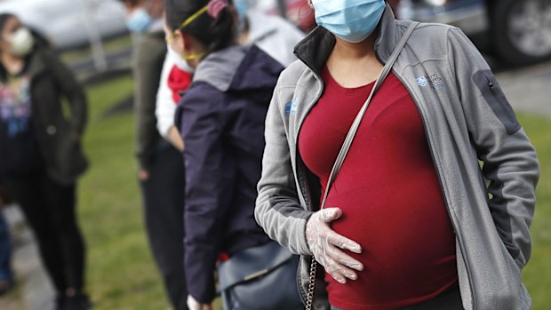  In this Thursday, May 7, 2020 file photo, a pregnant woman wearing a face mask and gloves holds her belly as she waits in line for groceries with hundreds during a food pantry sponsored by Healthy Waltham for those in need due to the COVID-19 virus outbreak, at St. Mary's Church in Waltham, Mass.