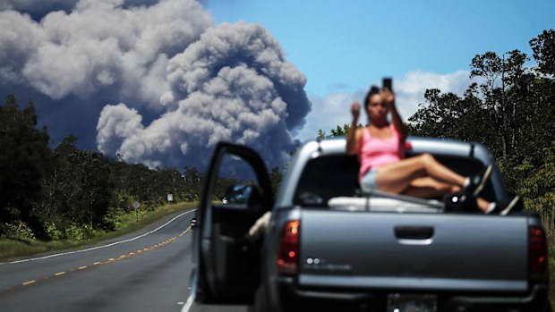 A woman takes a photo as an ash plume rises from the Kilauea volcano on Hawaii's Big Island on May 15, 2018.