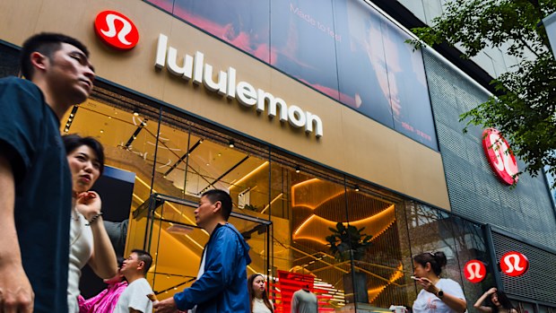 Pedestrians walk past a Lululemon retail store with its brand signage and interior displays visible through large glass windows.