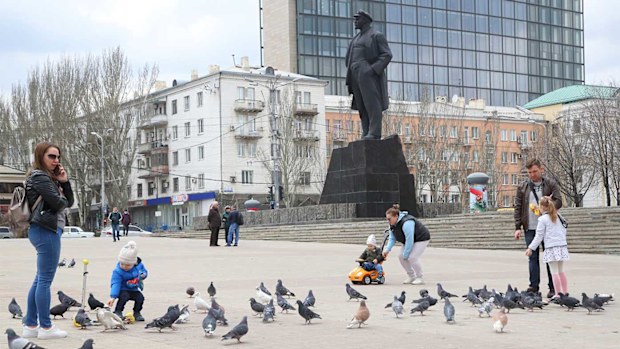People with their children walk in a square in front of statue of Vladimir Lenin in the separatist-controlled Donetsk, eastern Ukraine.