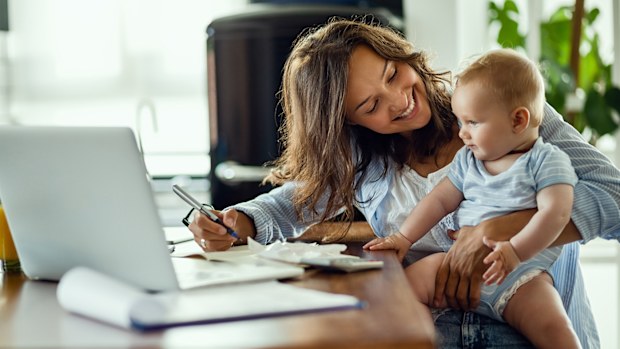 Work from home flexible work life working mum at desk holding baby juggling home work life balance