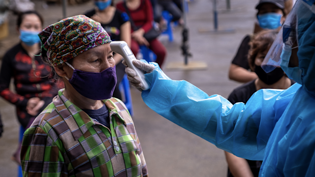 HANOI, VIETNAM - APRIL 18: A medical worker in protective suit takes temperature of a labourer from Long Bien market before taking the coronavirus disease (COVID-19) rapid test on April 18, 2020 in Hanoi, Vietnam. 