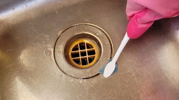 Woman cleans kitchen sink drain hole with a toothbrush