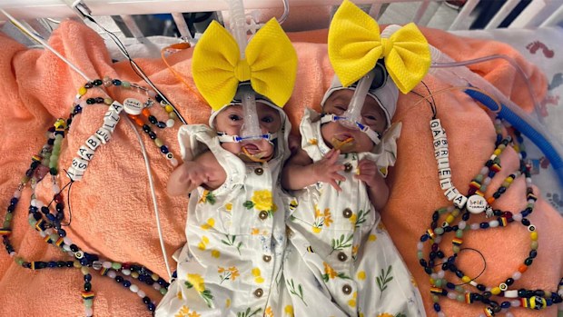 Premature twins in yellow outfits hooked up to machines in the NICU.