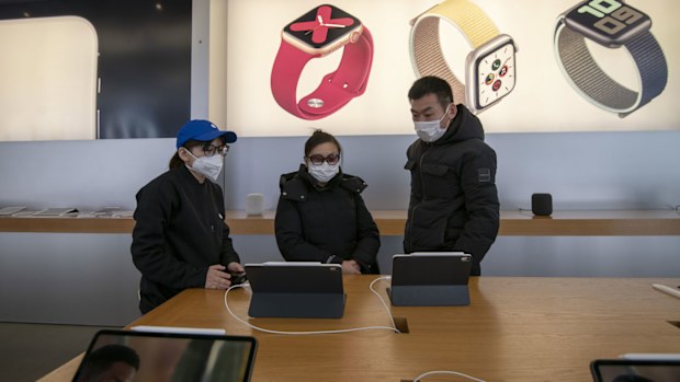 A female sales person in a blue baseball cap with an Apple logo and a protective mask shows iPads to a male and female couple insdie the Apple Store in the Xintiandi commercial precinct. 