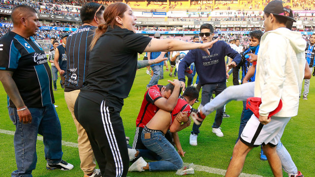 Fans of Atlas and Queretaro fight on pitch during the 9th round match between Queretaro and Atlas 