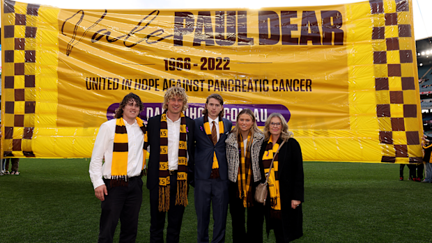 The family of late Paul Dear pose for a photo in front of the Hawks' banner ahead of their round 18 match in 2022.