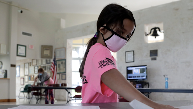 Valentina Fasano cleans her work space with sanitizing wipes at the Girl's Empowerment and Mentoring (G.E.M.) Summer Arts Camp during the coronavirus pandemic, Wednesday, July 15, 2020, in Miami. This Miami-Dade County summer camp program is operating at limited capacity, and has enhanced health screening and sanitizing procedures, practices social distancing, and required wearing of face coverings. (AP Photo/Lynne Sladky)