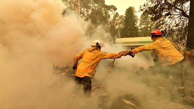 Firefighters hose down a burning woodpile during a bushfire in Werombi, 50km south west of Sydney, Friday, December 6, 2019.