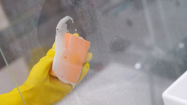 Cleaning the shower glass door with a sponge and soapy water