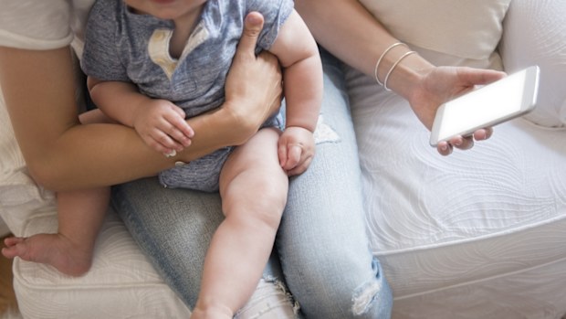 Mum holding baby on couch with iphone