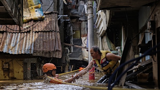 An Indonesian rescue worker helps his colleague as they navigate through a flooded neighbourhood on January 2, 2020 in Jakarta, Indonesia. 