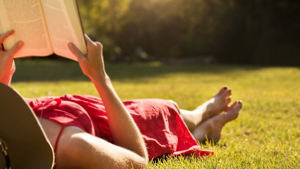 Shot of a young woman lying on grass and reading a book