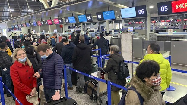Travellers wearing face masks stand in line at the check-in counters for Cathay Pacific at Shanghai Pudong International Airport in Shanghai.