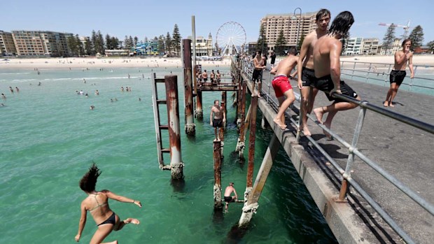 Teens jump of the jetty at Glenelg beach during a hot day in Adelaide.