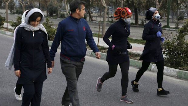 Two women jog with face masks on as others walk while enjoying their weekend afternoon at Pardisan Park in Tehran, Iran, Friday, Feb. 28, 2020