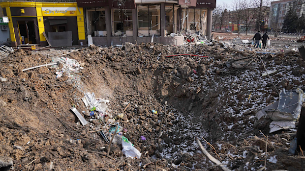  People walk past a crater from the explosion in Mira Avenue (Avenue of Peace) in Mariupol, Ukraine, Sunday, March 13, 2022. 