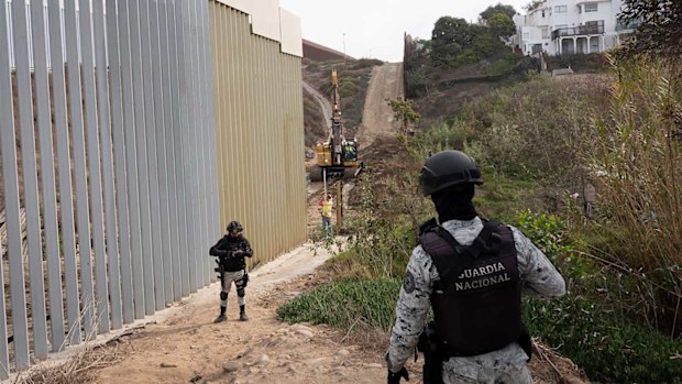Members of the Mexican National Guard watch as a section of the border fence is upgraded.