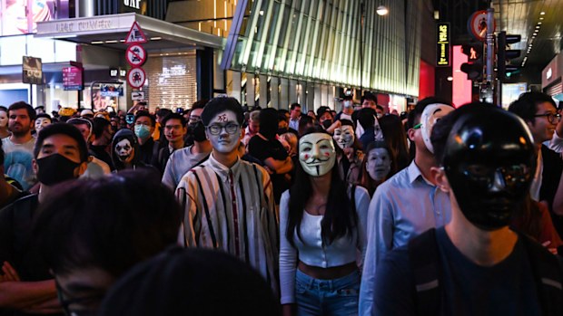 People in Guy Fawkes masks gather on the street during Halloween celebration.