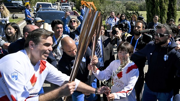 Second torchbearer, Japanese former marathon runner Noguchi Mizuki, passes the Olympic flame to the third torch bearer, European Commissioner Margaritis Schinas