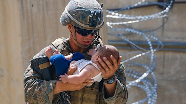 A US Marine assigned to 24th Marine Expeditionary Unit comforts an infant while they wait for the mother during an evacuation at Hamid Karzai International Airport in Kabul.