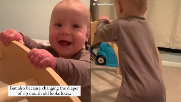 Baby standing holding on to furniture and smiling.