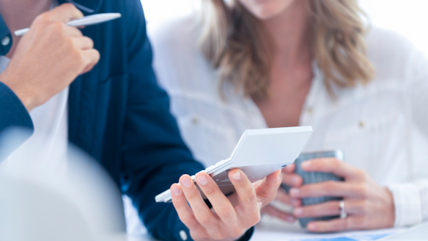 Young Couple working on their home finances. They are working at the dining room table using a calculator. There is some paperwork on the table. Close up tight crop. (Young Couple working on their home finances. They are working at the dining room tab