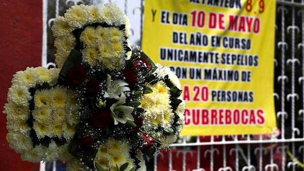 A funeral wreath is displayed at the entrance of the San Isidro cemetery near a sign that reads in Spanish: "There will be no access to the cemetery on May 8, 9 and 10" in Mexico City, Friday, May 8, 2020.  (AP Photo/Fernando Llano)