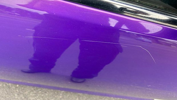 A purple car which has been damaged on one of its doors.