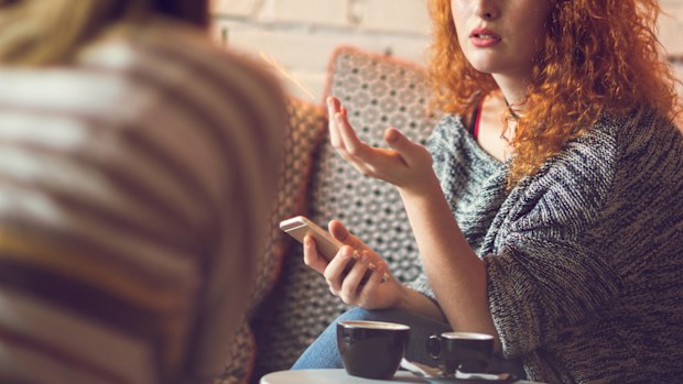 Young red-haired woman sitting in a cafe with friend and talking about something.